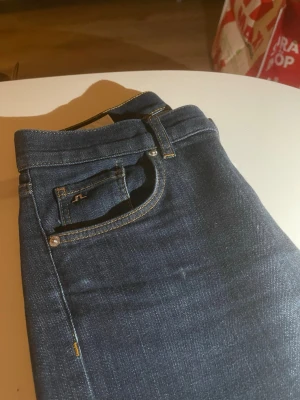 Mörkblå jeans från J.Lindeberg - Snygga mörkblå jeans från J.Lindeberg med klassisk femficksdesign och diskreta kontrastsömmar. Jeansen har en rak passform och är tillverkade i mjukt denimtyg som sitter skönt hela dagen.