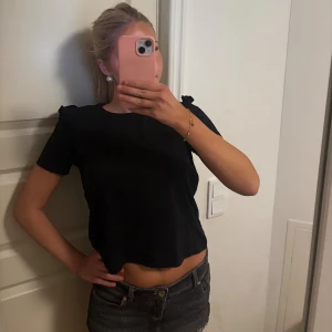 Svart  topp med volangdetalj - Säljer en svart topp med korta ärmar och volangdetaljer på axlarna. Storlek M men passar även S bra🩷