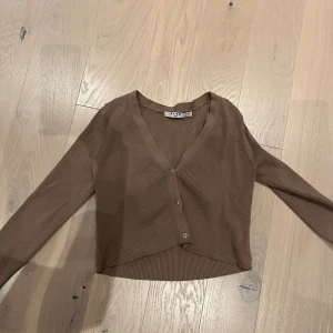Beige croppad ribbad topp från NA-KD - Säljer en beige croppad topp från NA-KD med ribbad struktur och v-ringning. Toppen har långa ärmar och knappar framtill. Passar bra till hösten! 🍂