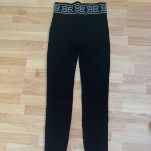 Svarta leggings med logotypresår XS - Svarta leggings med bred resår i midjan och vit logotypdetalj. Tillverkade i en stretchig mix av polyester, polyamid och elastan som sitter tajt och bekvämt. Perfekta för en sportig look eller chill vardagsstil.