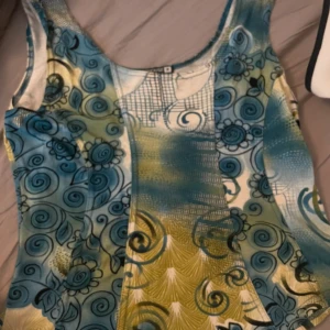 Färgglad mönstrad klänning Wearhouse - Säljer en topp från Wearhouse med unikt blått och grönt tyg swirliga och blommiga detaljer i tyget. Perfekt för dig som gillar färg och vill sticka ut. Materialet känns mjukt och stretchigt.