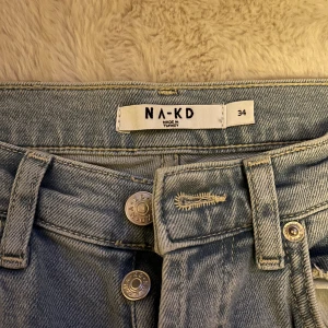Ljusblå raka jeans från NA-KD - Säljer ett par ljusblå jeans från NA-KD i klassisk rak modell. Jeansen har hög midja, fem fickor och knäppning med metallknappar framtill. Perfekta för en chill och stilren look. Materialet är robust denim i bomull.