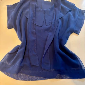 Blå blus med volangkrage Margit Brandt - Säljer en blå blus från Margit Brandt i luftig polyester. Blusen har korta ärmar, volangkrage och en lös passform. Perfekt för dig som gillar en stilren men ändå unik look. Märke syns i nacken och materialet är lätt och transparent.