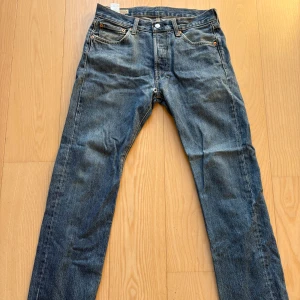 Levi's 501 blå jeans straight fit - Klassiska Levi's 501 jeans i blå denim med raka ben, normal passform och har ett hål vid skrevet.