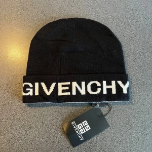 Svart Givenchy mössa med logga - Svart mössa från Givenchy med vit, stor logotyp framtill på uppvikt kant. Stilren och enkel design, perfekt för dig som gillar exklusiva märken. Materialet är mjukt och stickat, vilket gör den skön att bära under kyliga dagar.
