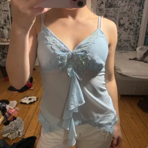 Ljusblå linnetopp med fjärilsdetalj - Supersöt ljusblå linnetopp med smala axelband och v-ringning. från romwe, aldrig använd och prislappen sitter fortfarande kvar, passar cs-s