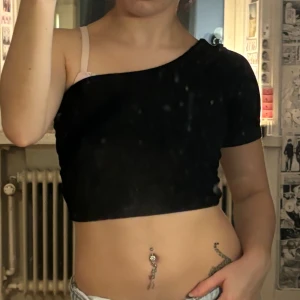 Svart croppad oneshoulder topp - Säljer en svart croppad topp med oneshoulder-design. T-shirten har kort ärm på ena sidan och är axelbandslös på andra, passar xs-s och är från shein