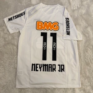 Vit Santos Neymar Jr fotbollströja Nike - Snygg vit fotbollströja från Nike med Santos FC klubbmärke, Neymar Jr och nummer 11 på ryggen. Tröjan har korta ärmar, svart Nike-logga och flera tryck i orange och svart. Materialet är lätt och andas, perfekt för match eller träning.