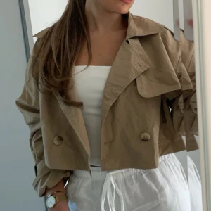 Beige croppad trenchcoat - Säljer en beige croppad trenchcoat i väldigt bra skick. Använd 2 gånger. Passar xs-s.