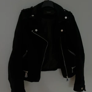 Svart skinnjacka från Vero Moda - Säljer en svart skinnjacka från Vero Moda med  silvriga dragkedjor och knappar. Jackan har snedställd dragkedja och flera fickor. Jackan är liten i storleken.