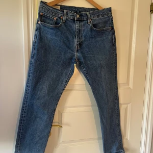 Levi's blå jeans W32 L30 - Klassiska Levi's jeans i blå denim med raka ben och normal passform. Byxorna har fem fickor, knappgylf och den ikoniska läderpatchen bak i midjan. Perfekta för dig som gillar tidlös stil och vill ha ett par jeans som funkar till allt.