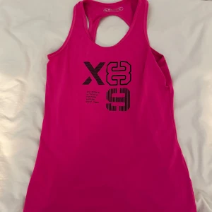Rosa träningstopp från SOC - Säljer en snygg och sportig rosa linnetopp från SOC i storlek 36. Toppen har brottarrygg och tryck framtill med siffror och text. Perfekt för träning och gjord i ett stretchigt syntetmaterial som andas. Enkel och stilren design som ger en fräsch look på gymmet.
