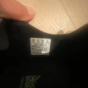 Puma svarta och gröna fotbollsskor strl 36 - Säljer ett par snygga fotbollsskor från Puma i svart med gröna och vita detaljer. Skorna har snörning, platt sula med dobbar och är tillverkade i syntetmaterial. Perfekta för dig som vill sticka ut på planen med stilren design och coola mönster.