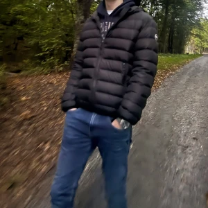 Colmar jacka svart - Säljer en svart pufferjacka med huva och dragkedja framtill. Jackan har en quiltad design med breda kanaler och snygg colmar logga på vänster arm, jackan är 100% äkta och det finns flera sätt att kolla upp det på. Jag är 182cm lång och väger 65