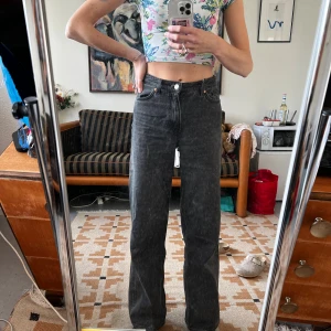 Svarta raka jeans med hög midja - Säljer ett par svarta jeans med hög midja och raka ben. Jeansen har klassisk femficksdesign och stängs med knapp och dragkedja. Materialet är denim och färgen är tvättad svart, vilket ger en cool och avslappnad vibe.