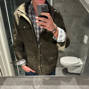 Olivgrön fieldjacket med dragkedja - Säljer en olivgrön parkajacka med flera fickor och silverfärgade knappar. Jackan har hög krage, dragkedja och tryckknappar framtill perfekt till hösten. Jackan är i riktigt bra skick. Jag är 188cm och bär storlek M. Hör av er vid funderingar;)
