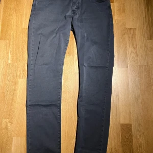 Mörkgrå byxor från Neuw - Snygga mörkgrå byxor från Neuw med klassisk femficksdesign och diskret logga på bakfickan. Byxorna har rak passform och är tillverkade i ett mjukt bomullsmaterial med lite stretch för extra komfort. Perfekta för en clean och stilren look.      | Perfekt skick