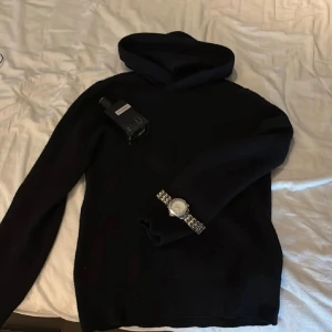 Svart hoodie i merinoull från Vailent XS - Svart hoodie från Vailent i 100% merinoull. Tröjan har lång ärm, huva och en clean, enkel design utan synliga detaljer. Perfekt för dig som gillar stilrena och bekväma plagg med premiumkänsla.