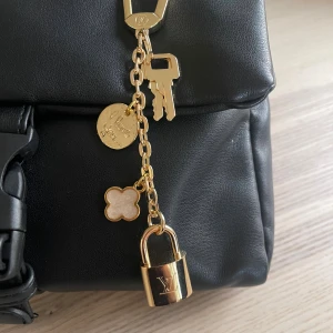 Perfekt att fästa på väskan eller som accessoar till guldigt nyckelberlock - Superfin  nyckelberlock i guldigt metall med hängande detaljer: två nycklar, ett runt mynt med texten 'I love you', en vit blomformad charm och ett klassiskt -hänglås. Perfekt att fästa på väskan eller som accessoar till nyckelknippan.