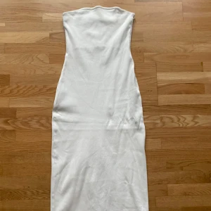 Vit långklänning från H&M Divided - Säljer en vit, ärmlös långklänning från H&M Divided. Klänningen är figurnära med slits baktill och har en enkel, stilren design. Materialet är ribbat och stretchigt vilket ger en snygg passform. Perfekt för dig som gillar minimalistisk stil.