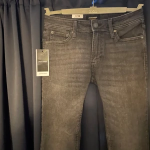 Grå  jeans från Jack & Jones - Snygga grå jeans från Jack & Jones med klassisk femficksdesign och smal passform. Jeansen har en mörkgrå tvätt och raka ben med något smalare avslut. Perfekta för dig som gillar en stilren och modern look. Strl30:30