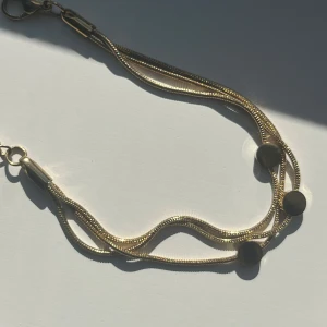 Guldigt armband med runda detaljer - Snyggt armband i guldton med dubbla tunna kedjor och tre runda, platta detaljer. Kedjorna har en mjuk, vågig form och armbandet stängs med en klassisk karbinhake. Perfekt accessoar för att lyfta din outfit.