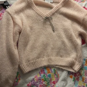 Ljusrosa stickad tröja från Vila - Supermysig ljusrosa stickad tröja från Vila i storlek M. Tröjan har v-ringning med en söt snörning och ribbade muddar vid ärmslut och nederkant. Perfekt för kyliga dagar och har en croppad passform som ger en trendig look. 