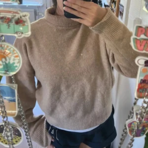 Beige polotröja i stickat material - Mysig beige polotröja i stickat material med ribbade muddar och hög krage. Tröjan har en loose passform och långa ärmar, perfekt för lager-på-lager under kyliga dagar.