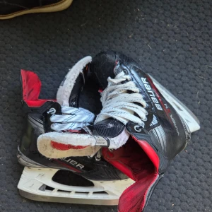 Bauer Vapor X 4 skates svart/röd - Säljer ett par Bauer Vapor X hockeyskridskor i svart och rött med vita snören. Skridskorna har en sportig design med robust konstruktion och detaljer i syntetmaterial. Perfekta för dig som vill ha snabba och smidiga skridskor på isen.