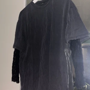 Svart t-shirt med spetsärmar  - Svart baggy t-shirt från Monki i storlek XS med coola spetsdetaljer på ärmarna. Klassisk rund hals och kortärmad design, men med transparent spets på ärmarna💕ALDRIG ANVÄND. Nypris 430 kronor