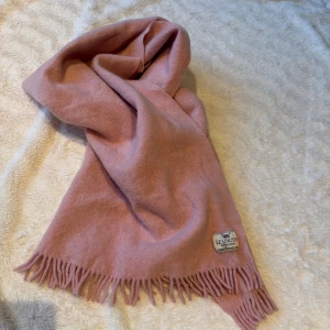 Rosa ullhalsduk från Lexington - Mysig och stilren rosa halsduk från Lexington med klassiska fransar i kanterna. Halsduken är tillverkad i mjuk ull och har en enkel, enfärgad design med en snygg Lexington-logga. Perfekt accessoar för kyliga dagar.