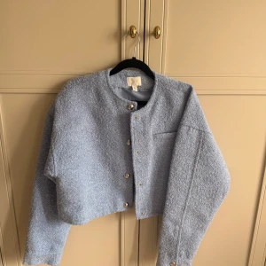 Ljusblå croppad  jacka - Snygg ljusblå croppad  jacka med rund hals och knappar framtill. 