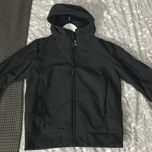 C.P company Shell R jacket  - Svart Shell R jacka från C.P. Company med huva, dragkedja framtill och två snedställda fickor med dragkedja. Skick 10/10 aldrig använd. Köpt för 5990 kr på NK i Stockholm. Självklart äkta, testa autentitet genom att scanna koden på lappen (bild 4). Priset kan diskuteras vid en snabb äffär 😎