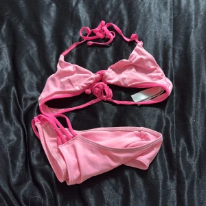 Rosa bikini med knyt - Snygg rosa bikini med trekantsöverdel och knyt i nacken och ryggen. Underdelen har smala band i sidorna för en trendig look. Perfekt för stranden eller poolen, och färgen poppar verkligen i solen.