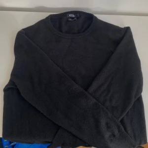 Svart kashmirtröja från Tiger of Sweden - Klassisk svart rundhalsad tröja från Tiger of Sweden i mjuk kashmir. Tröjan har lång ärm och är stickad i fin italiensk garn, perfekt för dig som gillar stilren och enkel design. Passar dig som vill ha en tidlös och snygg look.