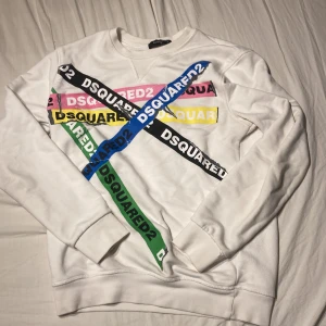 Vit DSQUARED2 sweatshirt med färgglatt tryck - Vit sweatshirt från DSQUARED2 i bomull med coola tryck i blått, grönt, rosa, gult och svart framtill. Tröjan har rund hals, långa ärmar och en relaxed passform. Perfekt statement piece för dig som gillar streetstyle och märkeskläder.