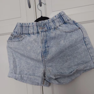 Ljusblåa högmidjade jeansshorts - ⚠️ Skriv till mig innan köp!⚠️Säljer ett par ljusblåa högmidjade jeansshorts med elastisk midja och klassisk femficksdesign. Shortsen har en tvättad look och uppvikta benslut för en avslappnad vibe. Perfekta för varma dagar och enkel att matcha med allt.