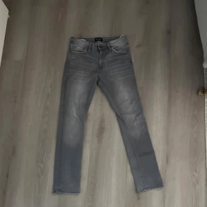 Slim fit grå jeans Glenn  - Snygga grå slim fit jeans från Glenn i storlek 30/32. Jeansen har klassisk femficksdesign, raka ben och en tvättad look med ljusare partier. Perfekta för dig som gillar en stilren och modern vibe.