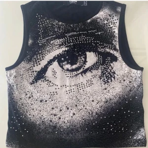 Jaded London svar vitt top - Jaded London ärmlös croptop med ett svart vit ögon print som är dekorerat med kristaller. Toppen är ganska stretchigt och skulle därför även passa väll pa en storlek M. Plagget har aldrig advents.