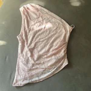 Ljusrosa spetsklänning från Gina Tricot - Superfin ljusrosa kortklänning från Gina Tricot med ett axelbandslöst snitt och blommig spets över hela tyget. Klänningen har en asymmetrisk form och känns både romantisk och trendig. Perfekt för dig som vill sticka ut med en söt och feminin look.