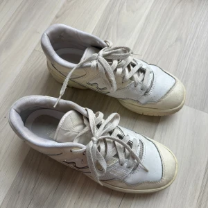 New Balance 550 vita sneakers strl 38 - Säljer ett par klassiska New Balance 550 sneakers i vitt och beige med snygga detaljer och snörning. Skorna har en rund tå, platt sula och är tillverkade i skinn och syntet. Perfekta för dig som gillar retrostil och vill ha bekväma sneakers med cool design.