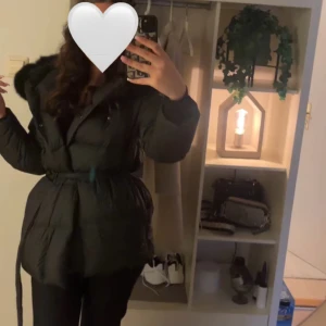 Svart dunjacka med äkta päls och bälte - Säljer en svart dunjacka med stor fluffig rävpäls på huvan och bälte i midjan. Jackan är quiltad och har en snygg, markerad siluett. Perfekt för kalla dagar när du vill vara både varm och stilren. Finns ett litet hål vid ena ärmen men inget som syns så jättemycket! Pris kan diskuteras‼️