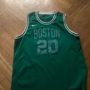Boston Celtics Hayward basketlinne Nike - Säljer ett grönt basketlinne från Nike med Boston Celtics-tryck och nummer 20, Hayward på ryggen. Linnet har vita detaljer vid hals och ärmhål och är tillverkat i ett lätt och ventilerande material. .