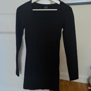 Svart långärmad kort klänning Gina Tricot - En stilren svart kort klänning från Gina Tricot i storlek S. Klänningen är kort, har lång ärm och rund halsringning. Tillverkad i ett mjukt och stretchigt material som sitter snyggt på kroppen. Perfekt basplagg att styla på många olika sätt.