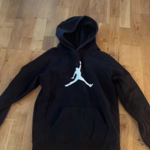 Svart Jordan hoodie med logga - Svart hoodie från Jordan med den klassiska Jumpman-loggan i vitt på bröstet. Tröjan har huva och en stor magficka framtill. Perfekt för dig som gillar sportig och avslappnad stil.