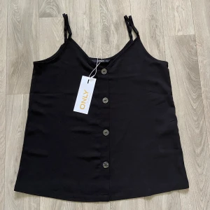 Svart linnetopp med knappar från ONLY - Svart linnetopp från ONLY med smala axelband och  knappar framtill. Toppen har en lätt strukturerad yta. Aldrig använd, nypris 199 kr🤍hör av dig vid frågor!
