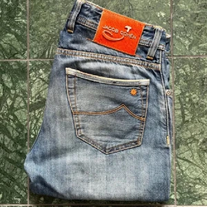 Jacob Cohen Jeans - Snygga limited edition jeans från Jacob Cohen med orange patch och unika detaljer. Klassisk blå tvätt, kontrastsömmar och knappar med brodyr. Tillverkade i japanskt denimtyg för en exklusiv känsla. Perfekta för dig som gillar premiumjeans med coola detaljer.
