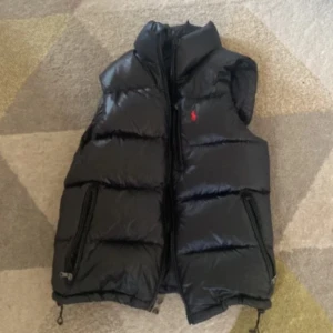Svart dunväst från Polo Ralph Lauren - Svart ralph lauren väst, säljer då den ej kommer till användning. Köpte den för 4600kr och den är knappt använd därför säljer jag den för 1250kr