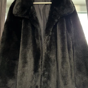 Svart pälsjacka från Woman's Wardrobe - Säljer en svart pälsjacka från Woman's Wardrobe i storlek 44. Jackan har en klassisk krage och är helsvart med mjuk, fluffig yta. Perfekt för dig som vill ha en snygg och varm jacka med lite lyxig känsla. Stängs framtill och har lång ärm.