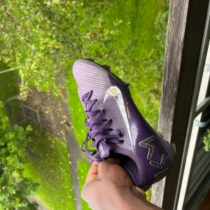 Nike Air Zoom fotbollsskor lila & gröna - Två par Nike Air Zoom fotbollsskor säljes. Ena paret är lila med silverfärgade detaljer och snörning, det andra är ljusgröna med svarta ränder och snörning. Båda har platt sula med dobbar för gräsplan och är tillverkade i syntetmaterial med mesh-ytor för extra ventilation.